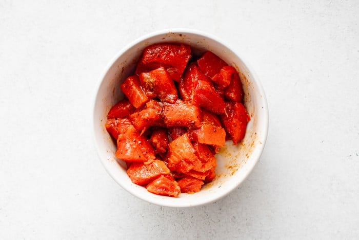 Raw salmon chunks coated in Cajun seasoning in a white bowl.