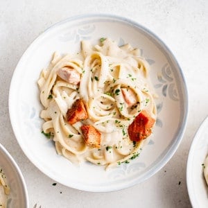 Three bowls filled with creamy salmon pasta arranged on a white surface.