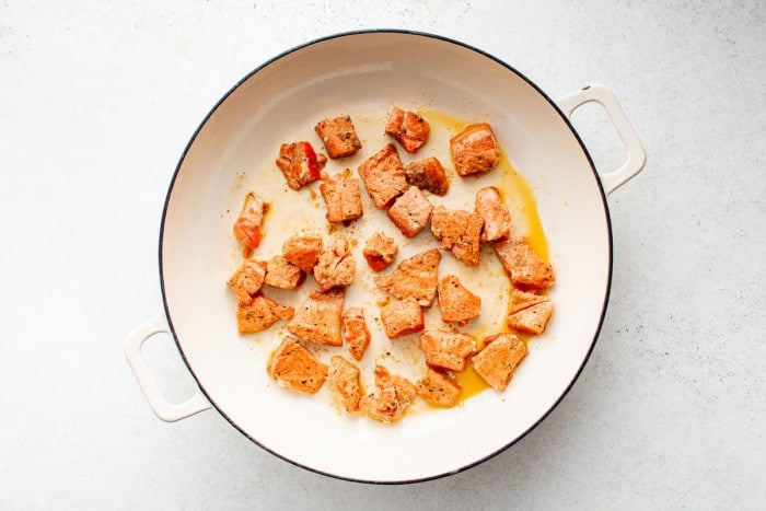 Searing Cajun-spiced cubes of salmon in a white skillet.