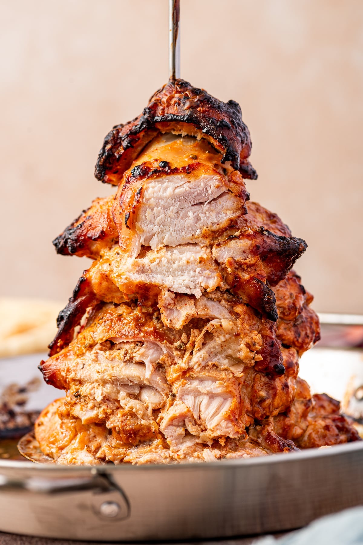 Close-up of chicken gyro meat sliced open on a vertical spit, showing juicy white chicken inside with orange spiced marinade, dark charred edges, and golden roasted pieces in a silver pan.