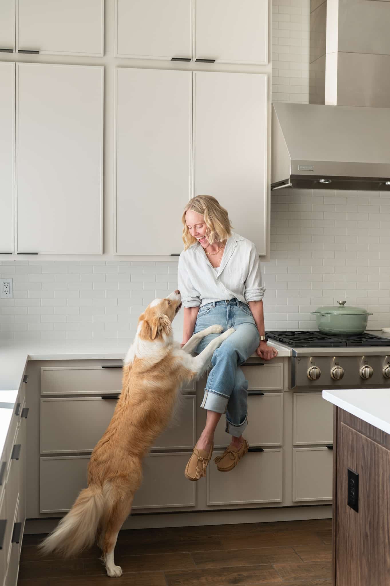 Chef Jessica Randhawa sitting on her kitchen counter with her dog Ash standing up to greet her.