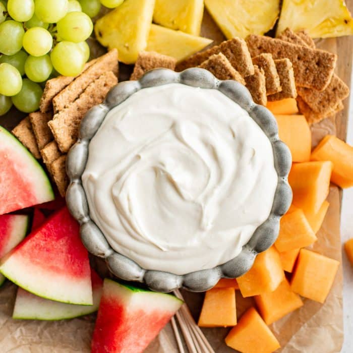 A fruit tray featuring a bowl of cream cheese dip surrounded by watermelon wedges, pineapple, grapes, cantaloupe cubes, and graham crackers.