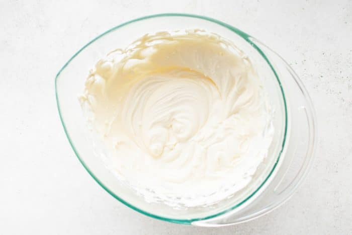 A glass mixing bowl filled with smooth and fluffy cream cheese fruit dip.