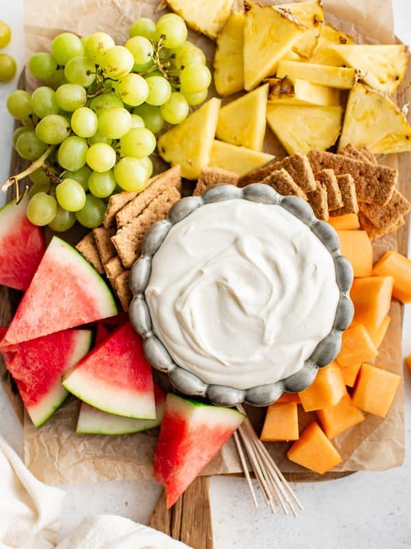 A fruit tray featuring a bowl of cream cheese dip surrounded by watermelon wedges, pineapple, grapes, cantaloupe cubes, and graham crackers.