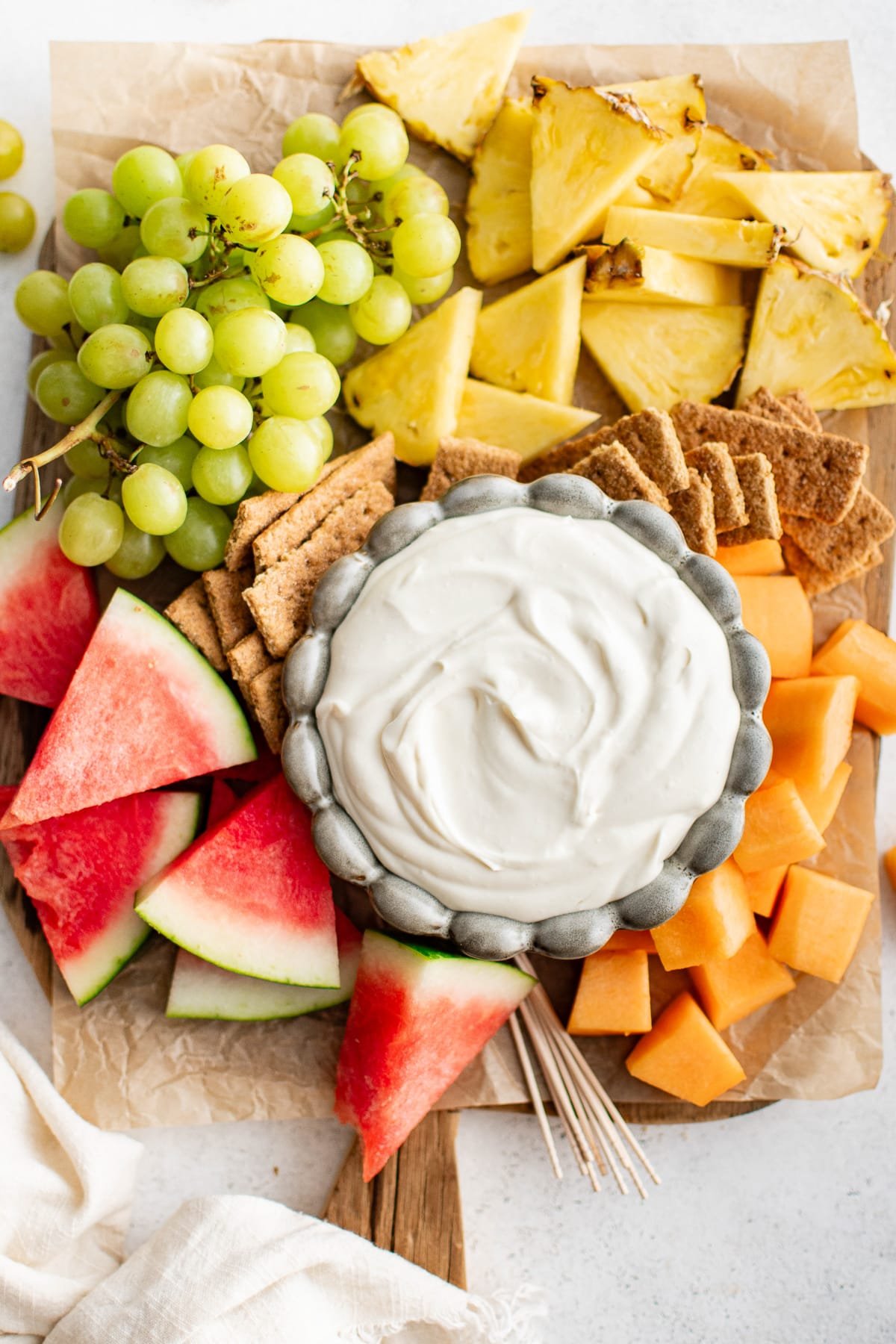 A fruit tray featuring a bowl of cream cheese dip surrounded by watermelon wedges, pineapple, grapes, cantaloupe cubes, and graham crackers.