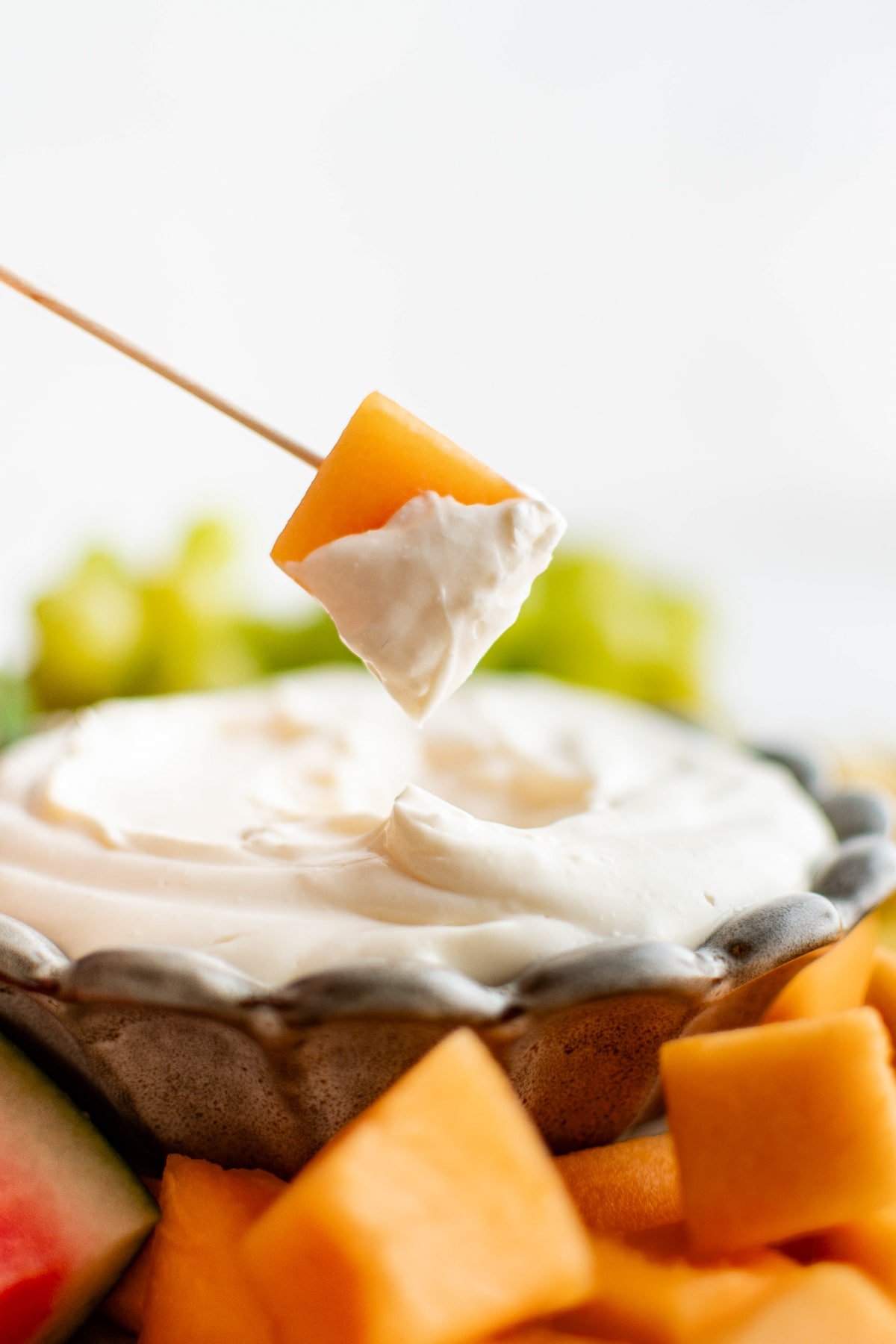 Cantaloupe cube dipped in cream cheese fruit dip on a wooden skewer.