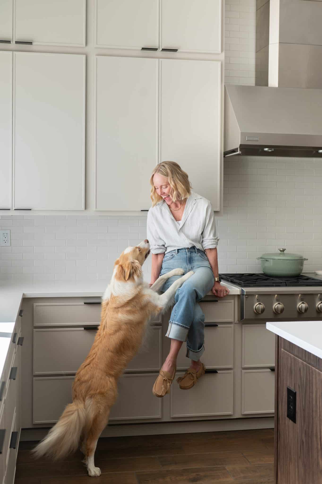 Chef Jessica Randhawa sitting on her kitchen counter with her dog Ash standing up to greet her.