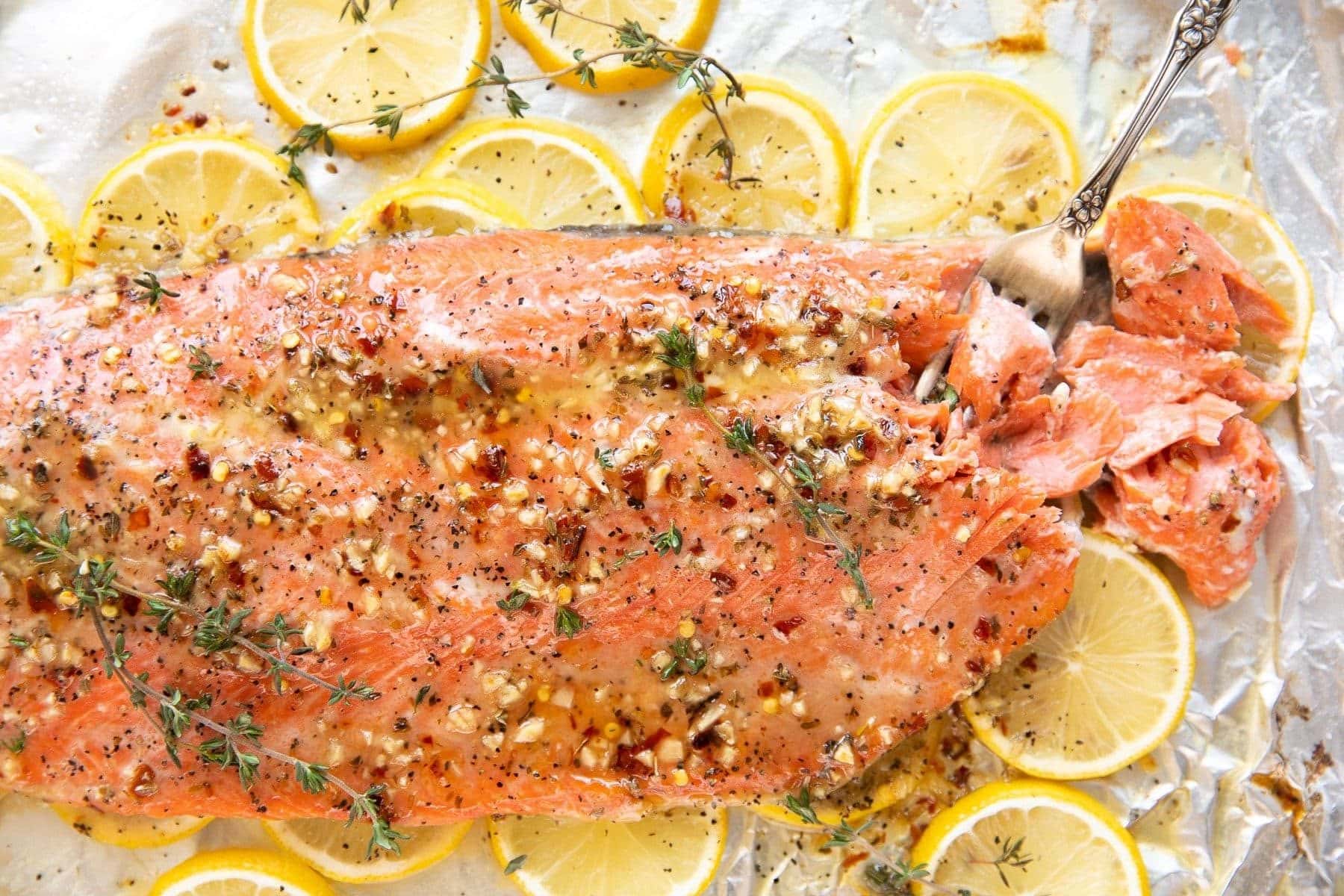 Close up image of baked salmon covered in a lemon butter sauce and garnished with fresh thyme.