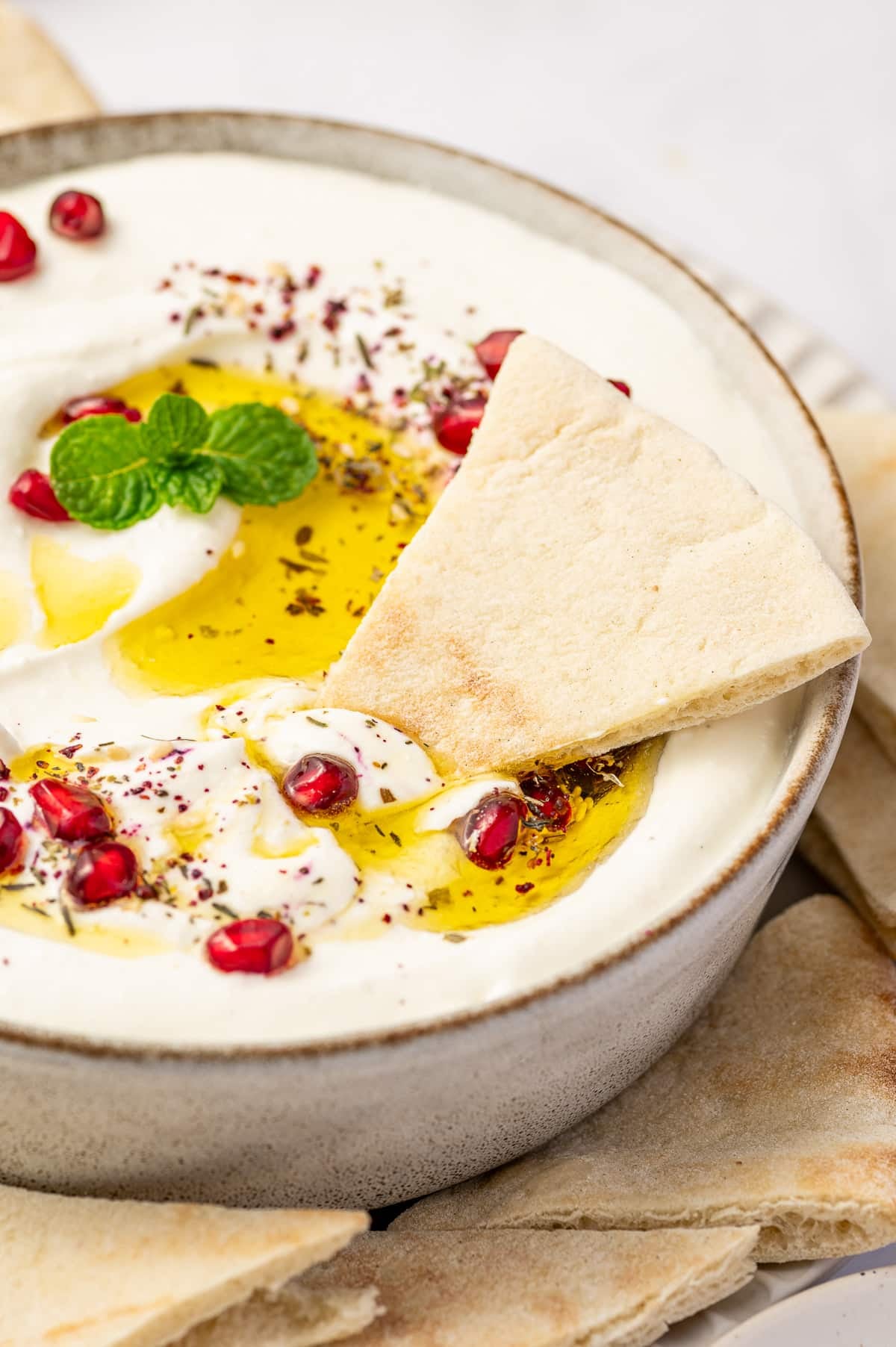 A close-up of warm pita dipped into whipped feta garnished with pomegranate, olive oil, and za’atar.