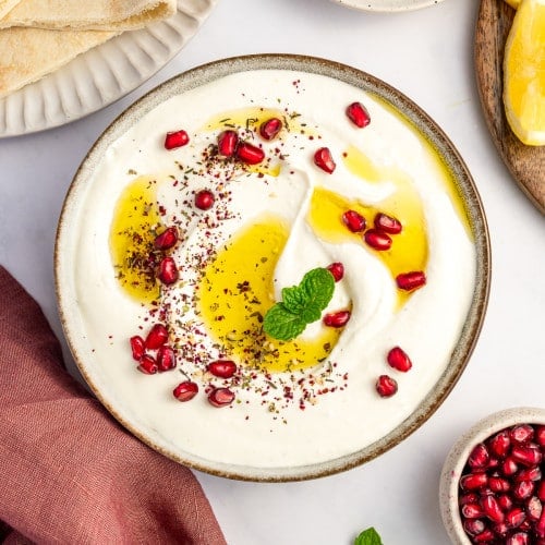 Styled flatlay of whipped feta dip surrounded by pita, za’atar, lemons, and fresh mint.