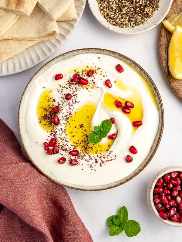 Styled flatlay of whipped feta dip surrounded by pita, za’atar, lemons, and fresh mint.