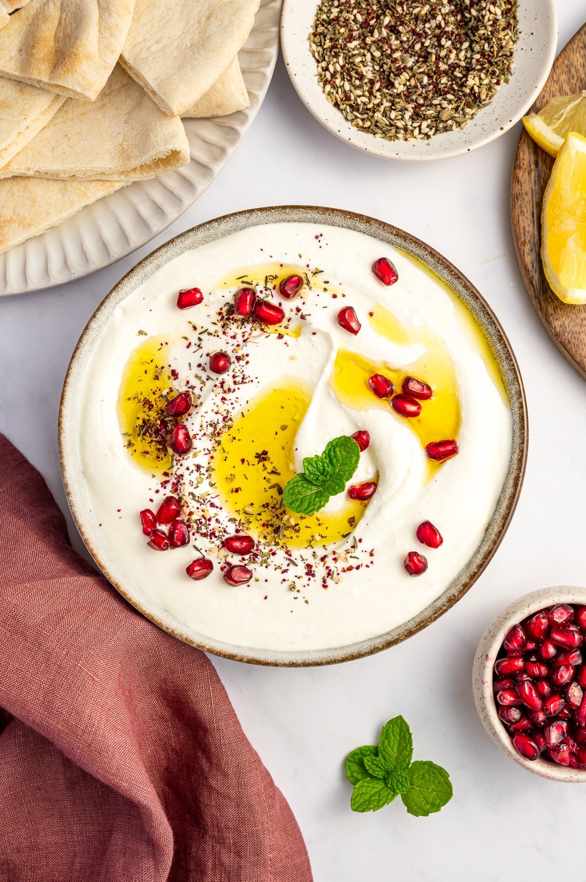 Styled flatlay of whipped feta dip surrounded by pita, za’atar, lemons, and fresh mint.