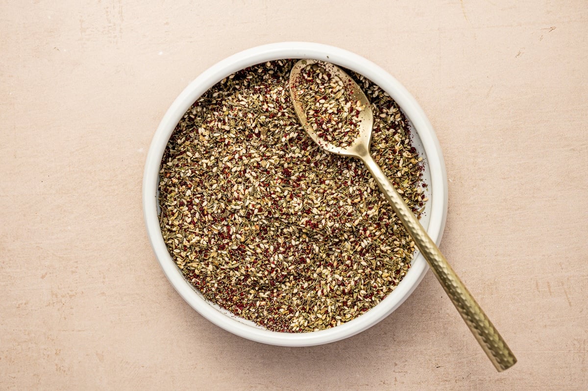 Finished homemade za’atar seasoning in a white bowl with a gold spoon.
