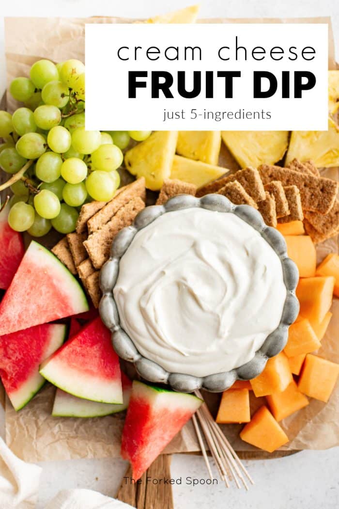 A top-down photo of a bowl of cream cheese fruit dip on a platter of watermelon, grapes, cantaloupe, pineapple, and graham crackers, with a title box overlay that reads "cream cheese FRUIT DIP just 5-ingredients."