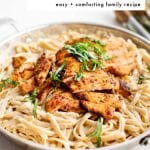 Sliced blackened chicken served over creamy fettuccine Alfredo in a skillet, topped with fresh basil, with text overlay that reads "Blackened Chicken Alfredo, easy + comforting family recipe."