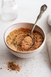 A close-up view of homemade blackened seasoning in a small bowl with a spoon. The seasoning is slightly mounded in the center, with a fine-textured mix of spices and herbs visible in detail.