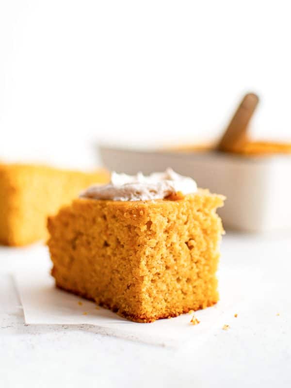 Moist and dense slice of sweet potato cornbread with a visible crumb structure, topped with cinnamon butter and set on white parchment.