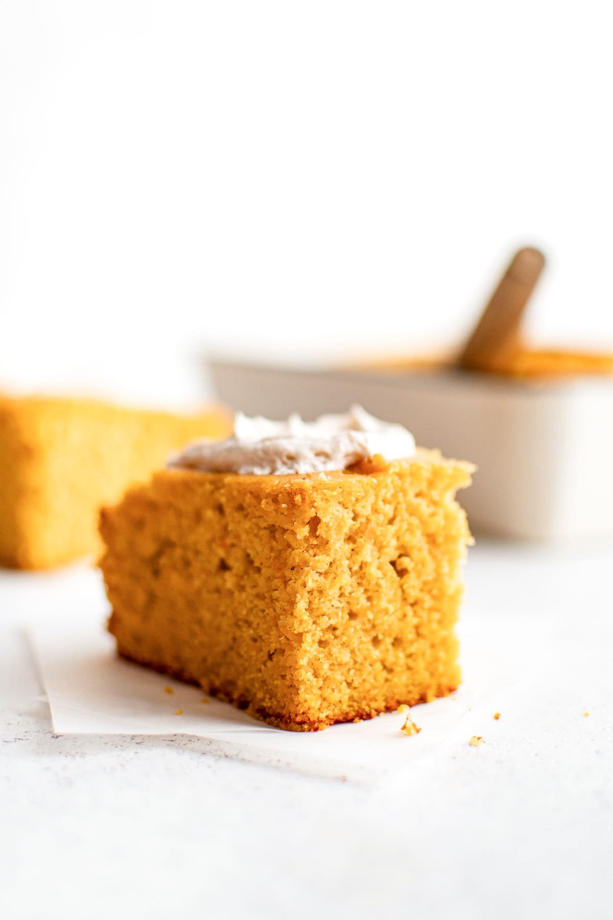 Moist and dense slice of sweet potato cornbread with a visible crumb structure, topped with cinnamon butter and set on white parchment.