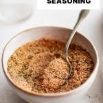 Vertical Pinterest pin featuring a bowl of mixed blackened seasoning with a spoon resting inside. The text Homemade Blackened Seasoning is displayed in bold uppercase font across the top portion of the image.