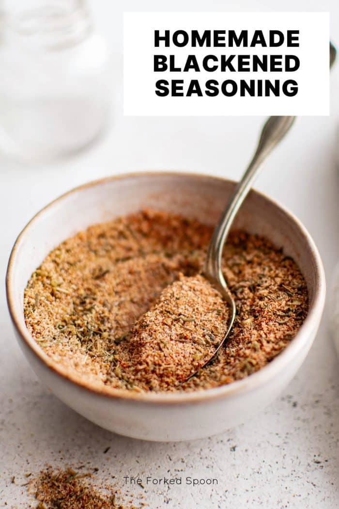 Vertical Pinterest pin featuring a bowl of mixed blackened seasoning with a spoon resting inside. The text Homemade Blackened Seasoning is displayed in bold uppercase font across the top portion of the image.