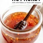 Pinterest graphic with text reading "How to Make Hot Honey with chili flakes or fresh chili peppers", featuring a glass jar of hot honey with a honey dipper resting inside.