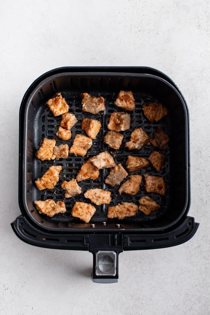 Fully cooked salmon bites in an air fryer basket, lightly caramelized from the glaze.