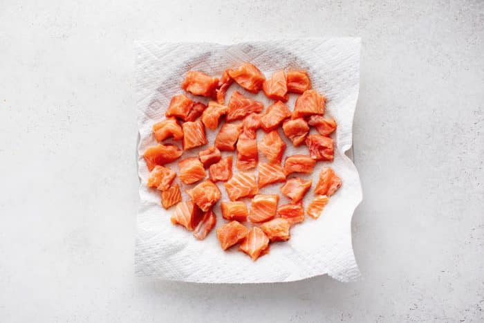 Cubes of raw salmon arranged on a plate lined with paper towels to remove excess moisture before cooking.