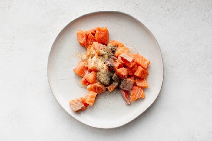 Salmon cubes on a plate topped with olive oil, garlic powder, onion powder, salt, and pepper.