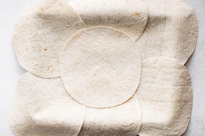 Overhead view of tortillas fully arranged on the buttered baking sheet with an additional tortilla placed in the center to cover gaps.