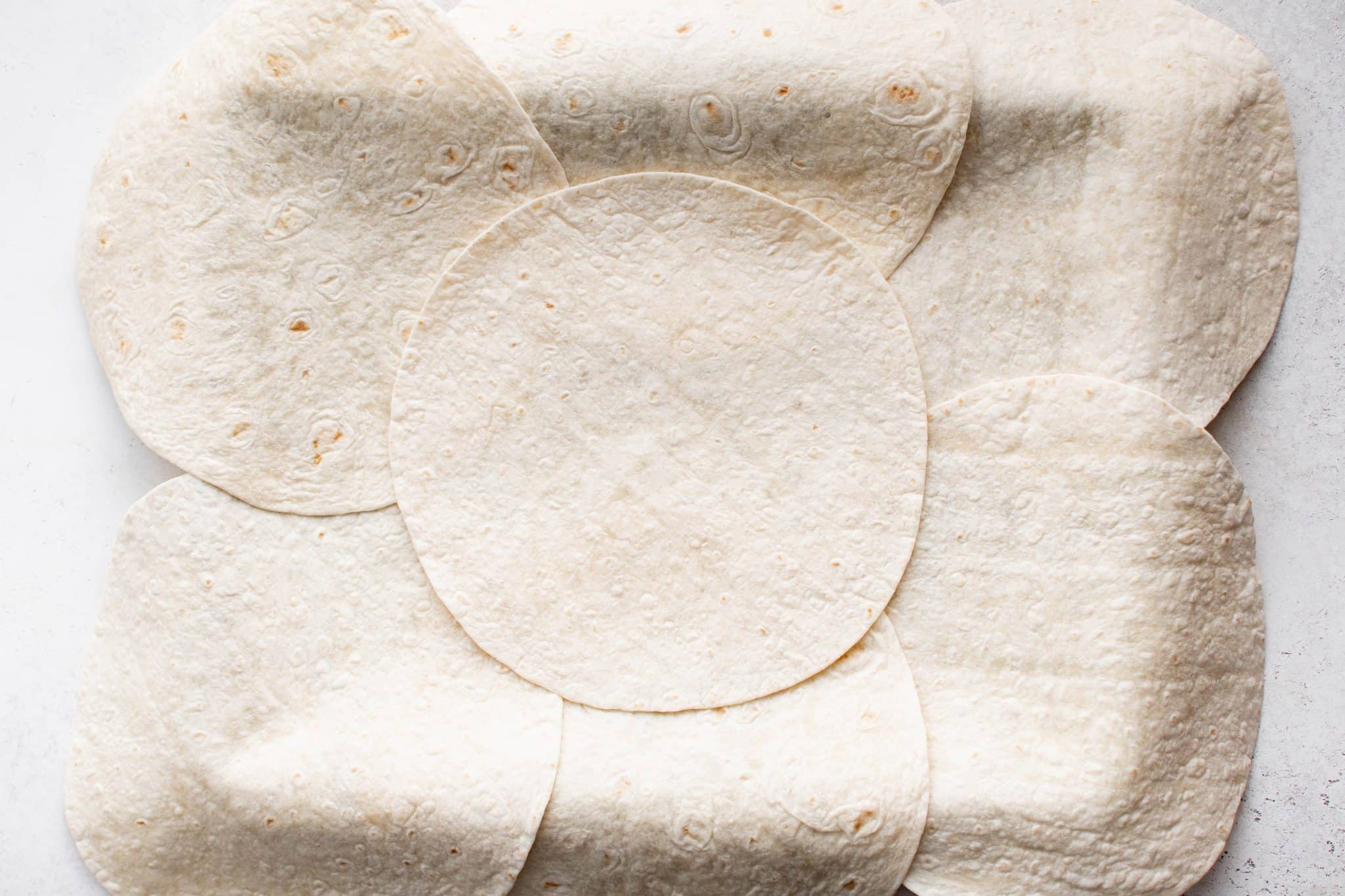 Overhead view of tortillas fully arranged on the buttered baking sheet with an additional tortilla placed in the center to cover gaps.