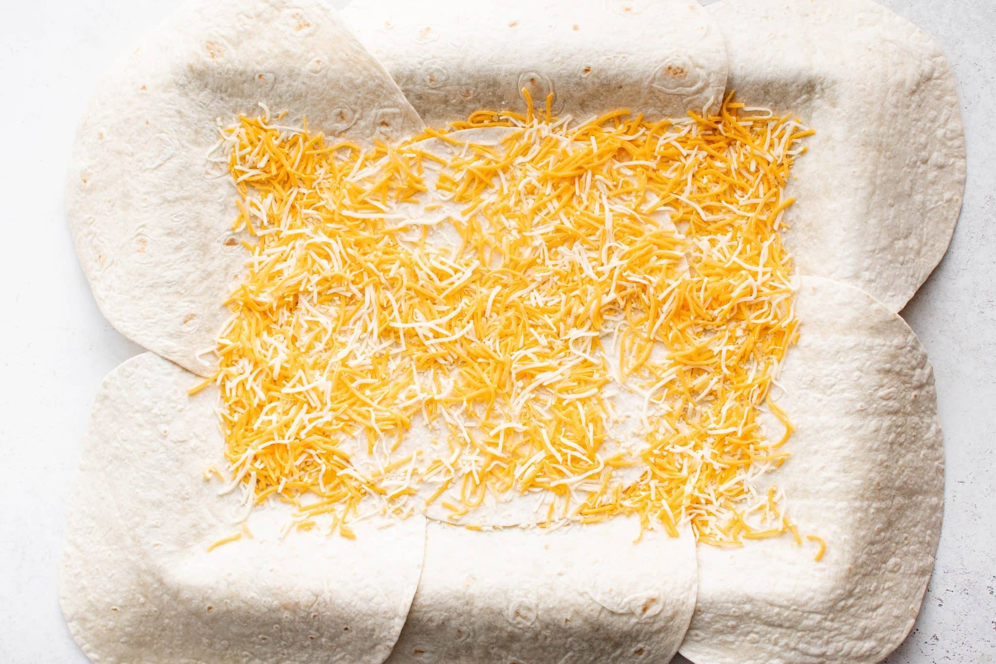 Overhead view of the tortillas on the sheet pan topped with an even layer of shredded Mexican blend cheese.