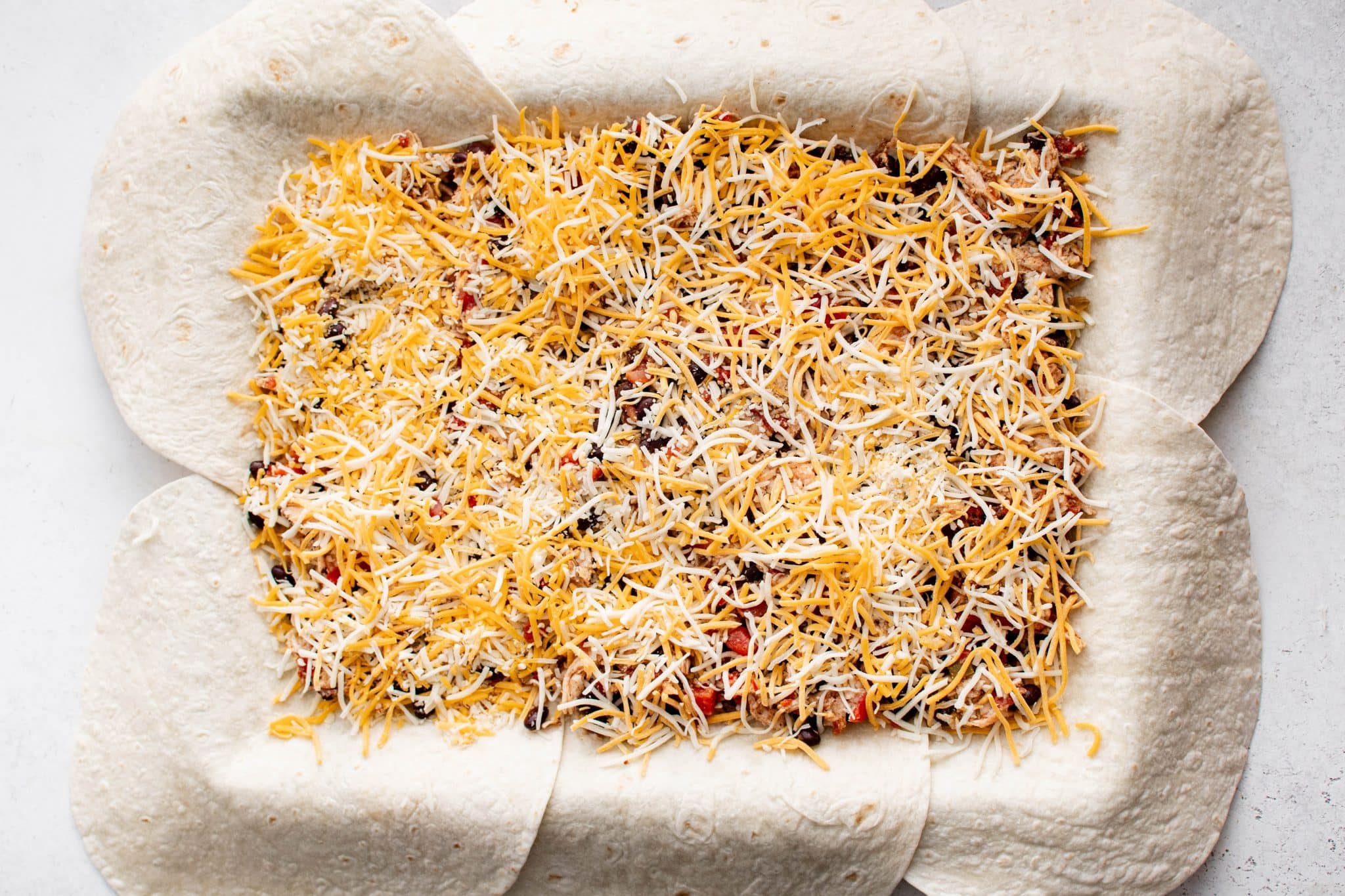 Overhead view of a second layer of shredded cheese spread over the chicken and bean filling in the sheet pan.