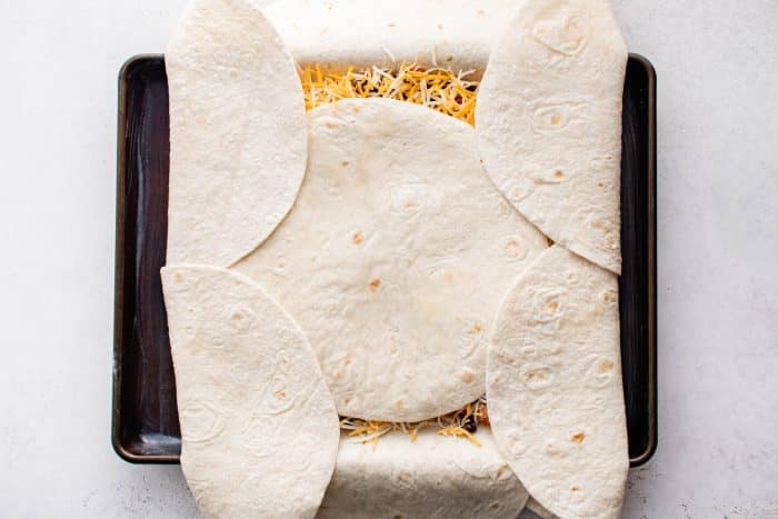 Overhead view of the overhanging tortillas folded inward over the filling, overlapping across the center tortilla to form a sealed top crust.
