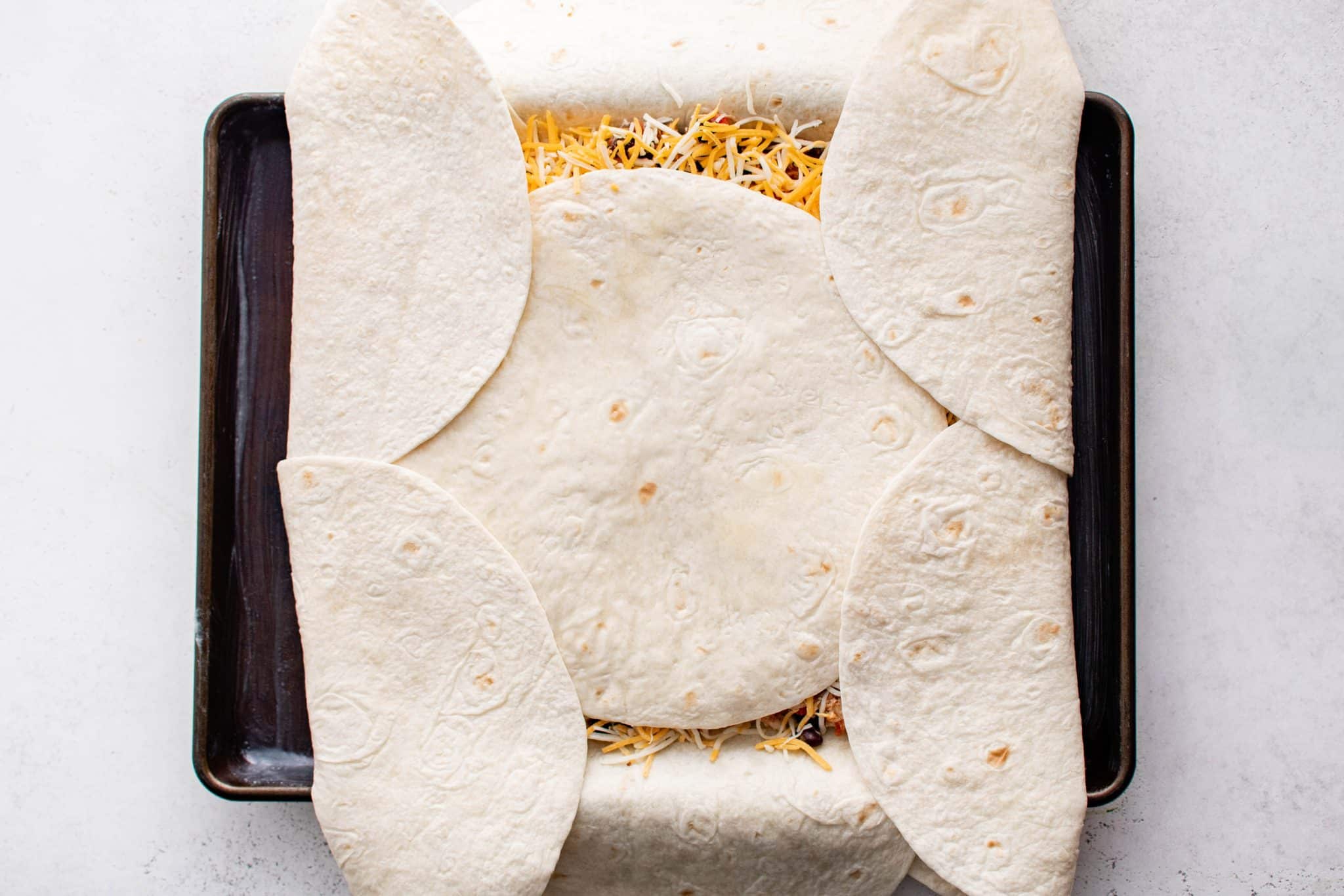 Overhead view of the overhanging tortillas folded inward over the filling, overlapping across the center tortilla to form a sealed top crust.