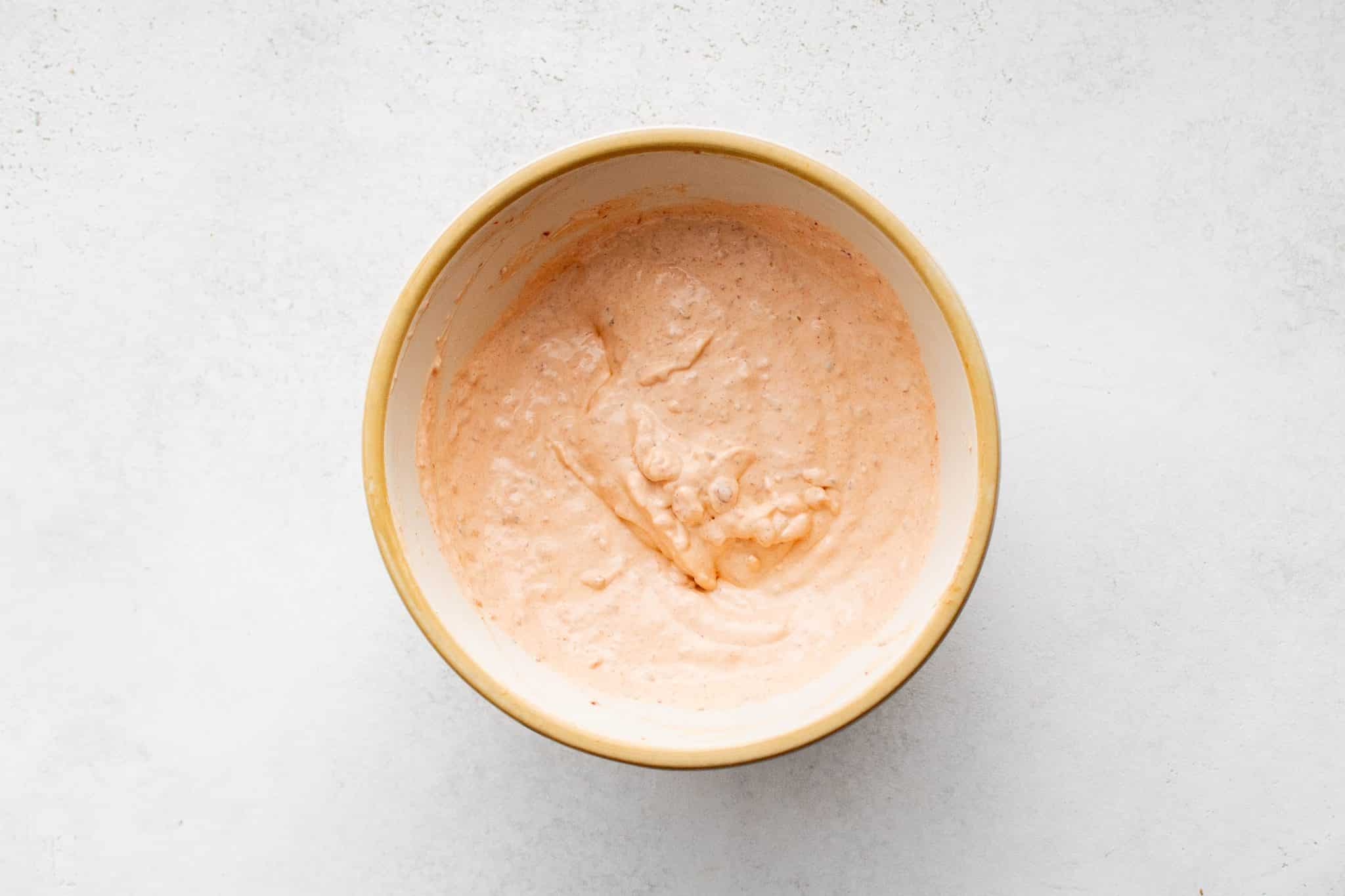 Overhead view of a bowl with the sour cream and chipotle pepper mixture whisked into a smooth, light orange chipotle crema.