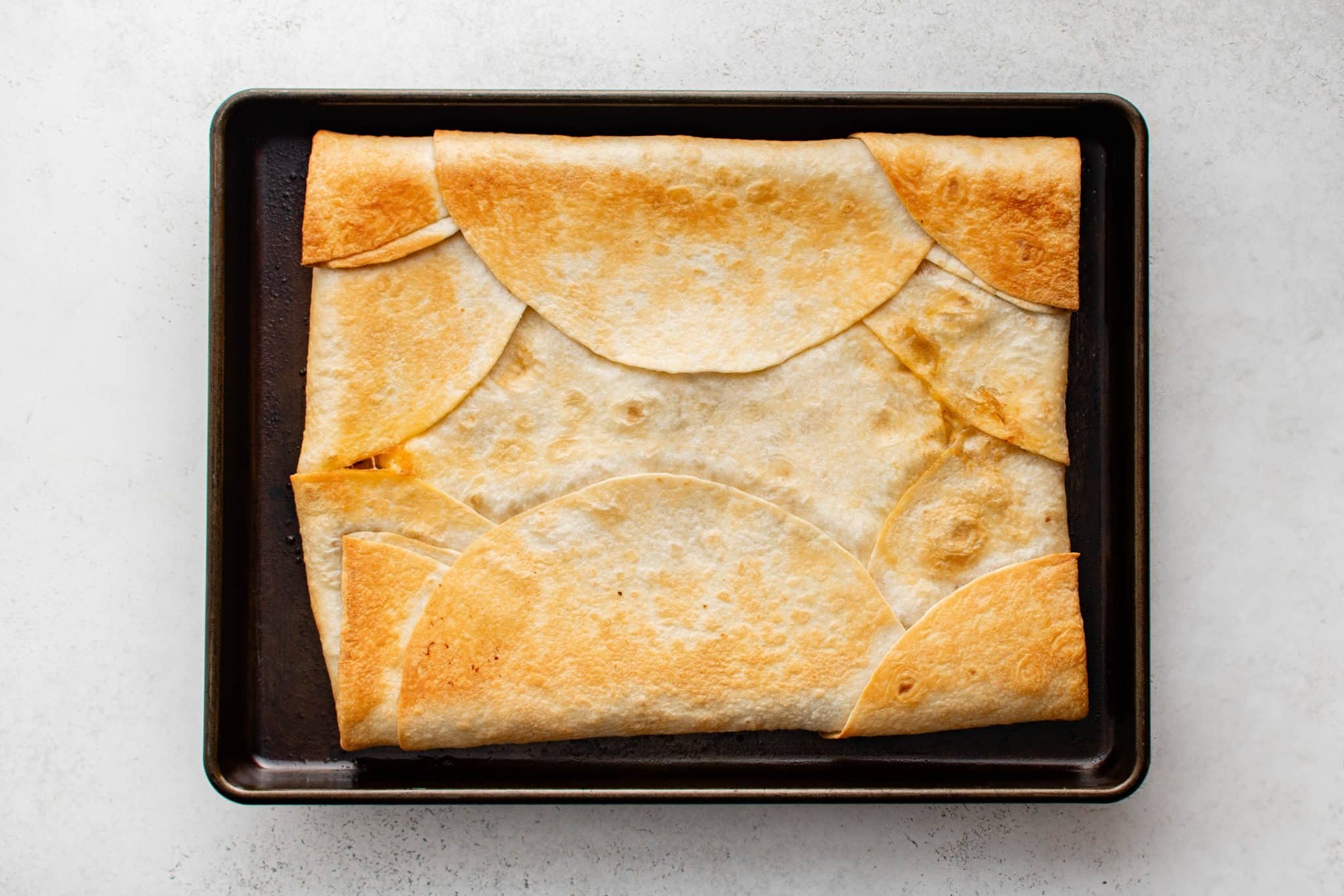 An overhead view of baked sheet pan quesadillas fresh from the oven, with the tortillas golden brown and crisp around the edges.