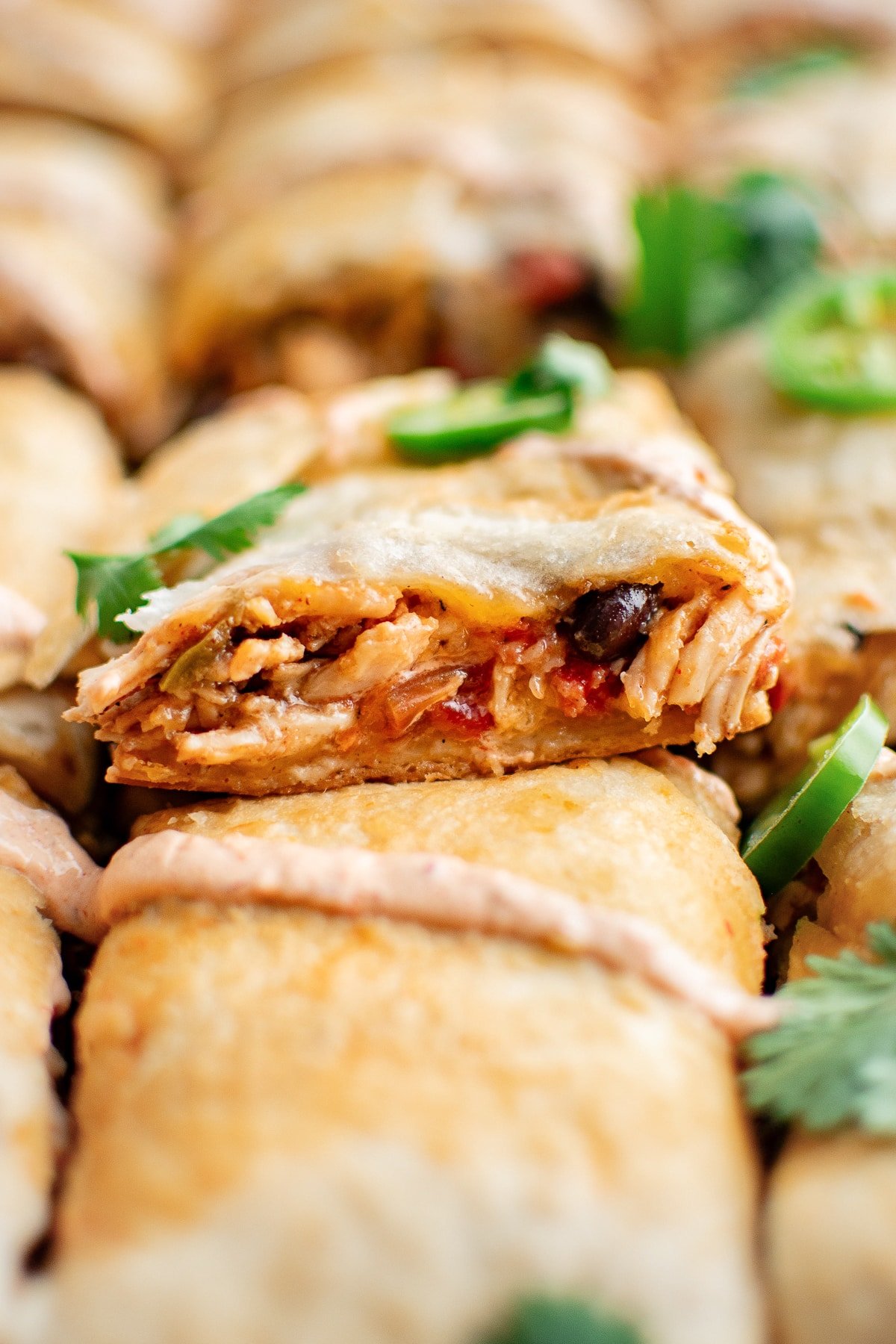 Close-up of a sliced quesadilla square lifted slightly to show the filling of shredded chicken, black beans, melted cheese, and tomatoes inside the golden-brown tortilla crust.
