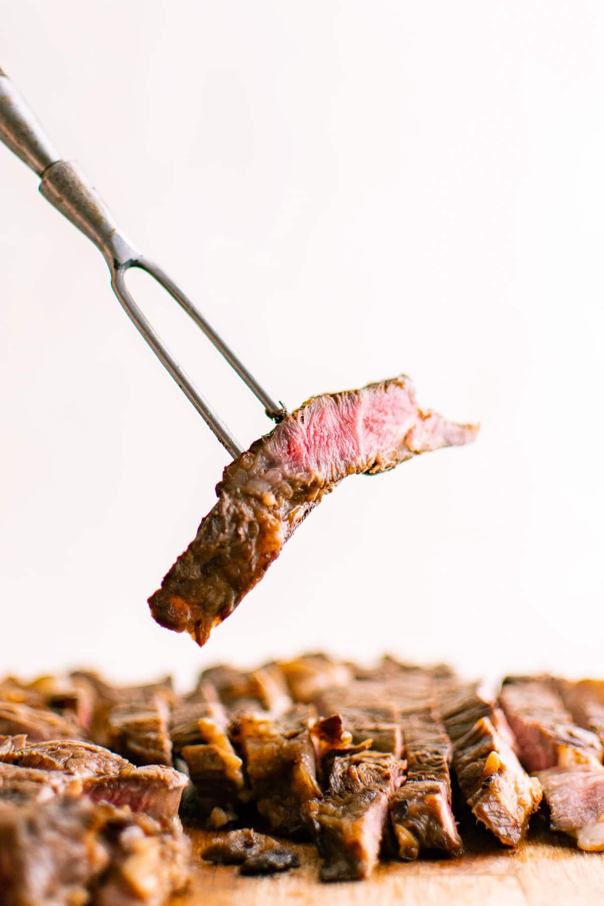 Single piece of sliced steak held up on a meat fork, showing the juicy pink center and seared brown exterior.