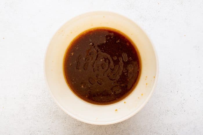 Bowl of steak marinade after ingredients have been whisked together, creating a smooth, dark brown mixture with visible oil droplets.