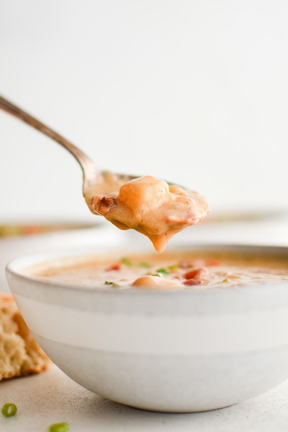 Close-up of a spoon lifting a hearty bite of beer cheese soup with melted cheese, potatoes, and bacon from a bowl.