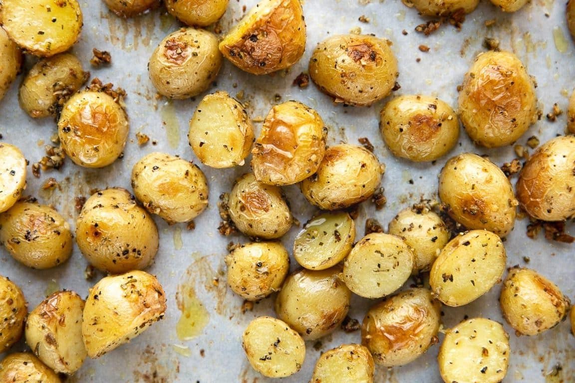 Roasted garlic baby potatoes on a large parchment-lined baking sheet with golden, crispy edges.
