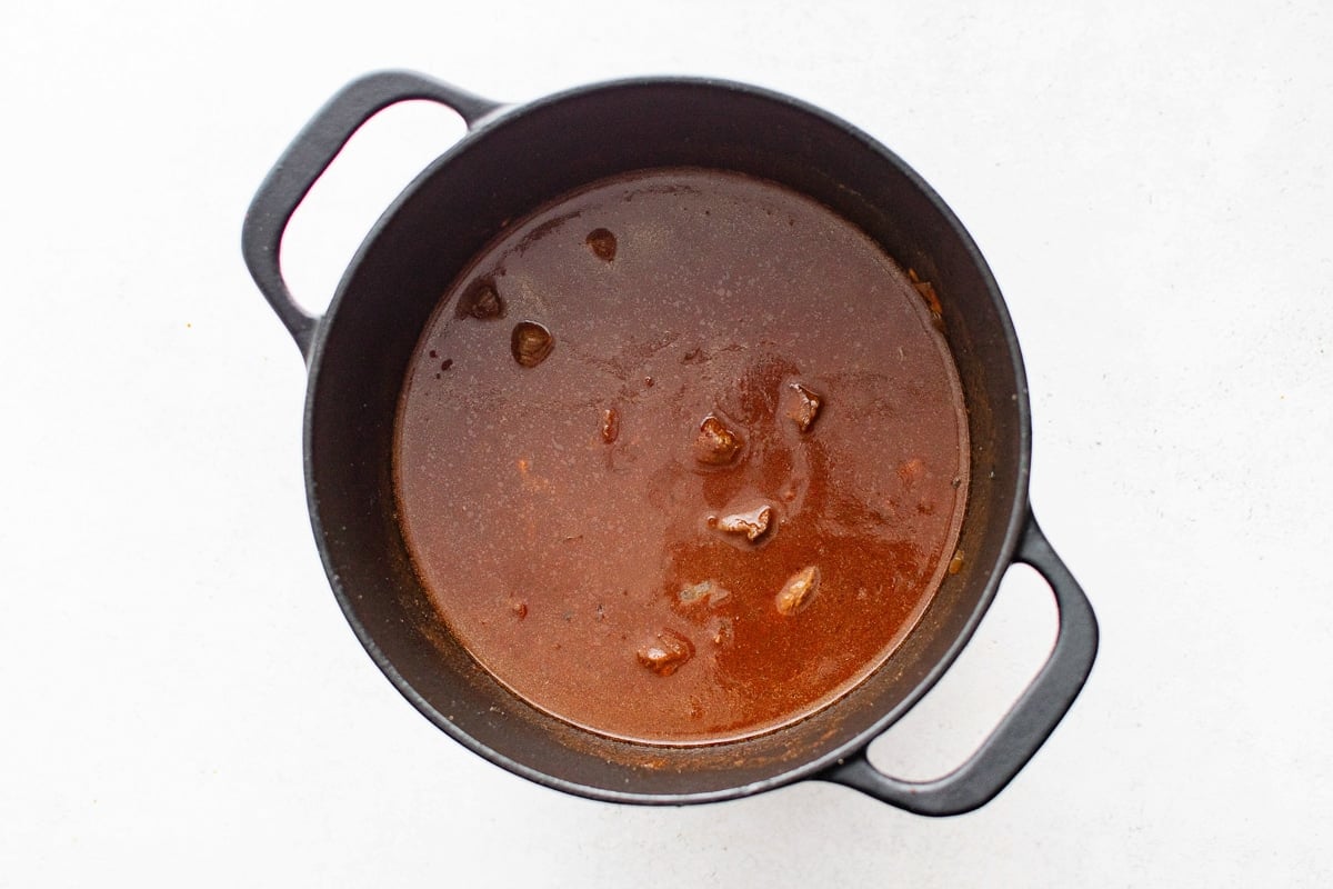 A pot of chili with beef cubes and a deep red broth, ready to simmer.