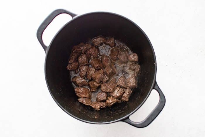 Cubes of chuck roast beef fully browned on the surface in a Dutch oven.