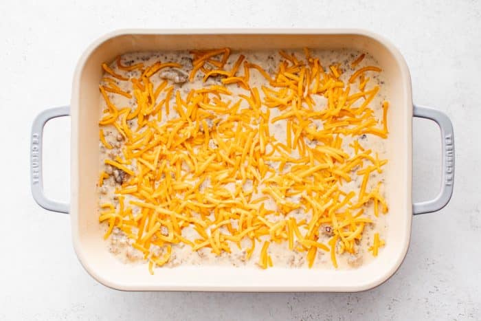 Shredded cheddar cheese sprinkled on top of sausage gravy in a casserole dish.