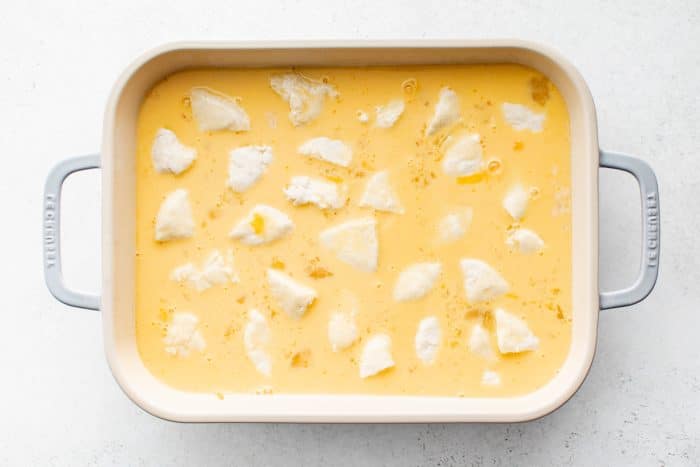 Whisked eggs and milk mixture poured over biscuits, cheese, and sausage gravy in a casserole dish.