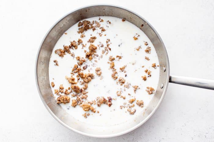 Cooked sausage in skillet with milk poured in to make creamy gravy for biscuits and gravy casserole.