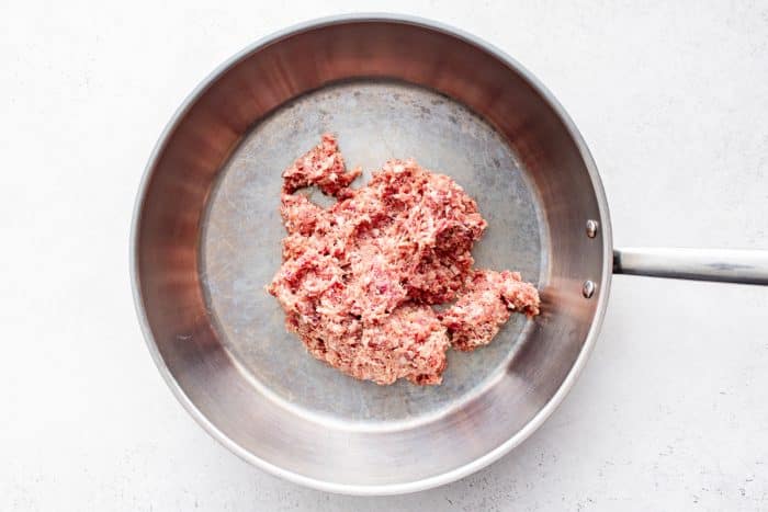 Raw breakfast sausage placed in a stainless steel skillet before cooking for biscuits and gravy casserole.