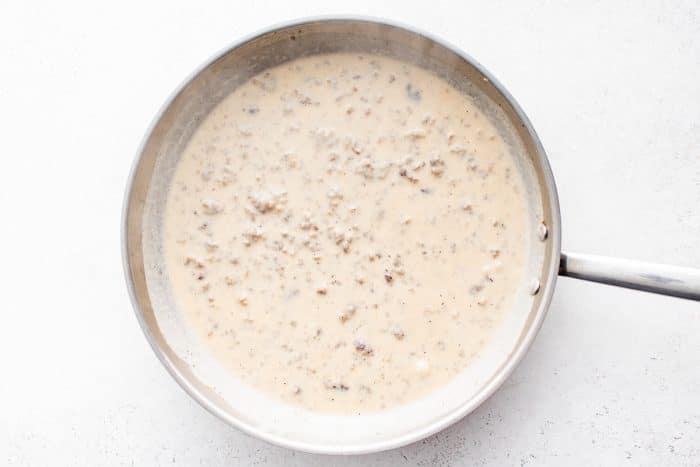 Creamy sausage gravy simmered in a skillet, thickened and ready to be poured into the casserole dish.