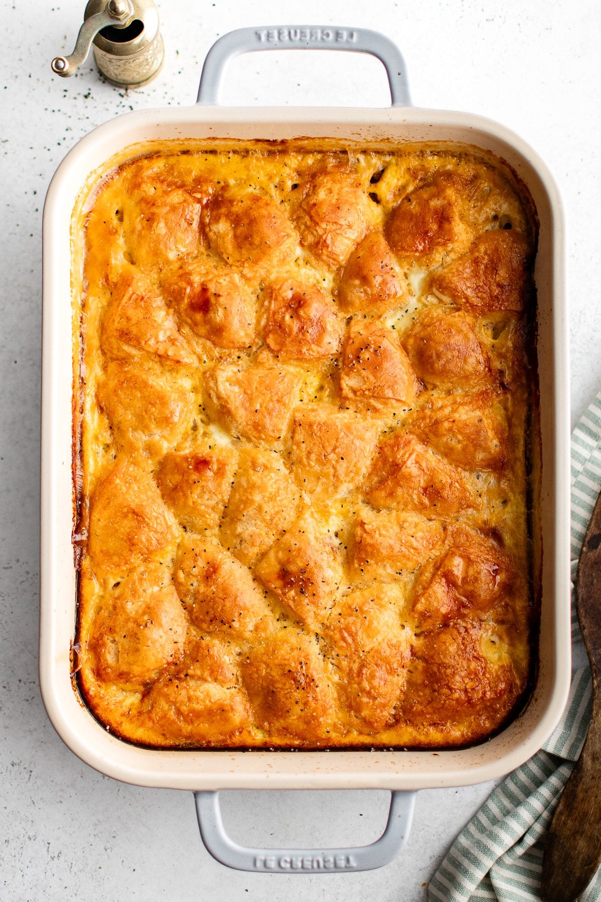 Golden baked biscuits and gravy casserole sprinkled with black pepper in a ceramic Le Creuset dish.