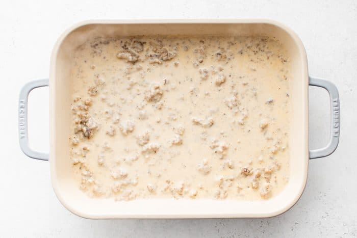 Homemade sausage gravy spread evenly in the bottom of a rectangular ceramic baking dish.